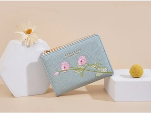 Detail shot of light blue wallet featuring pink floral embroidery and gold brand logo