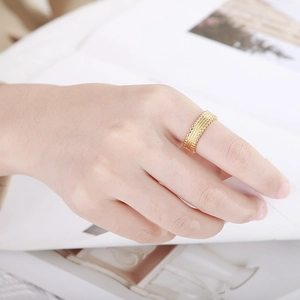 Detailed view of gold titanium ring with tire texture worn on finger over minimalist background