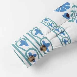 Détail de la manchette d'un manteau en coton blanc avec motifs floraux bleus et bouton