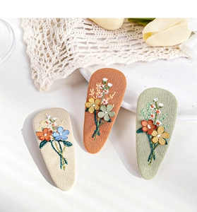 Detail of three drop-shaped floral embroidery hair clips in beige orange and green