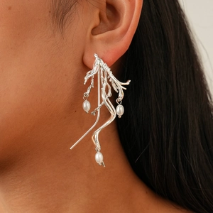 Close-up of irregular branch-like silver earrings with three elegant white pearls