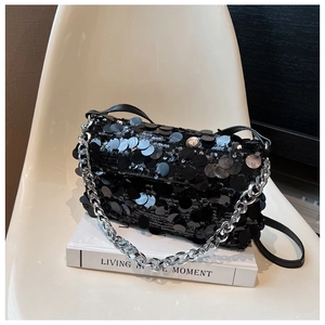 Detail of elegant black sequin evening bag with silver chain strap on a white book