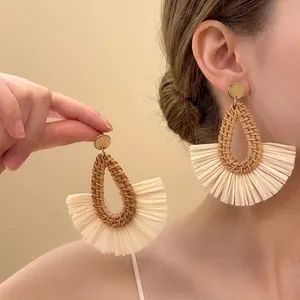 Detail of bohemian raffia drop earrings with golden studs and fringe accents