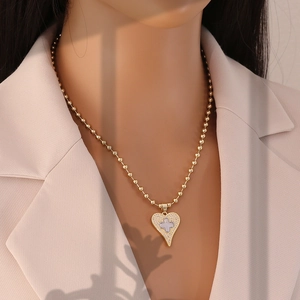 Detail view of heart pendant necklace with zircon cross on a model in a beige blazer