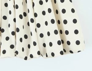 Detailaufnahme von weißem Stoff mit schwarzen Punkten und plissierter Saumstruktur