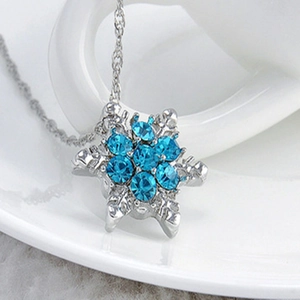 Silver snowflake pendant necklace with blue rhinestones displayed on a ceramic cup