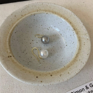 Elegant 18K gold pearl hook earrings in grey and white tones displayed in a ceramic bowl