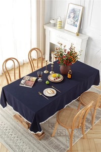 Detail of navy blue cotton tablecloth with decorative white pom-poms on a wood table
