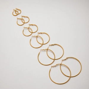 Set of seven different sized gold stainless steel hoop earrings on white background