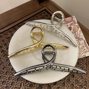 Three oversized metal hair claws in gold, silver, and gunmetal on a white plate