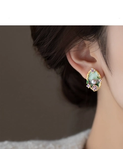 Detail of vintage gold-rimmed green enamel flower earrings with pearl on female model
