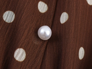 Détail macro du tissu mousseline à pois marron avec un bouton en perle blanche polie