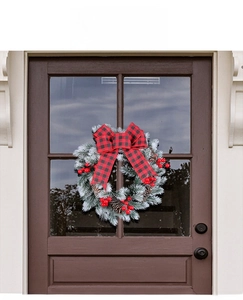 Close-up of frosted pine needles, red berries, and plaid bow on Christmas wreath