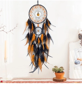Macro detail of handmade dream catcher with black and orange feathers on a white wall
