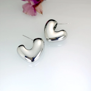 Macro shot of minimalist 3D silver heart earrings on a white reflective background
