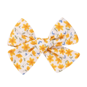 Close-up of fabric bow hair clip with yellow floral pattern on white linen texture