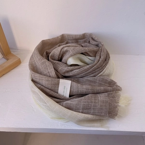 Close-up detail of beige and brown gradient scarf fabric with tassels and premium label