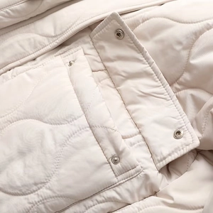 Close-up of wavy quilted pattern and polished metal snap buttons on cream cotton jacket