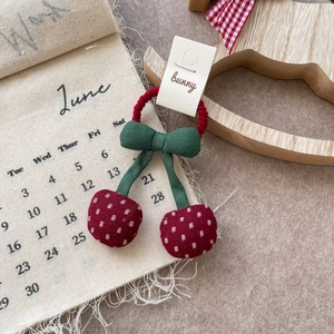 Detail of a sweet cherry fabric hair tie with polka dots and a green bow on soft fabric