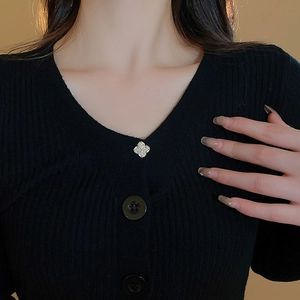 Detail of a gold clover brooch with white zircons pinned to a black striped cardigan