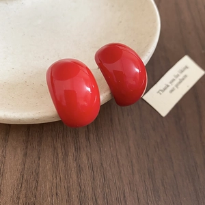 Close-up of glossy red teardrop stud earrings on a ceramic dish with high-shine finish