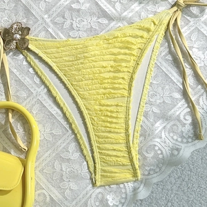 Detail of yellow bikini bottom featuring seersucker texture and floral side tie charm