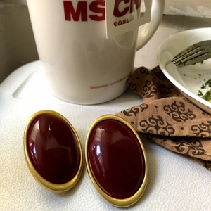 Vintage oval red resin stud earrings with golden metal frame on an aesthetic background