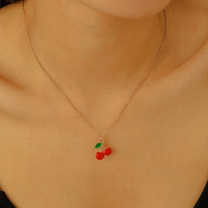 Close-up of golden cherry pendant necklace with red enamel and green leaf on skin