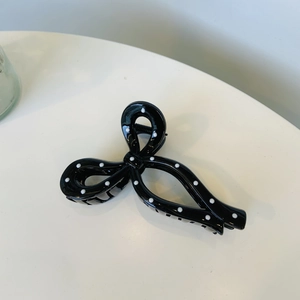 Detailed view of a black hair claw clip with white polka dots in a bow shape design