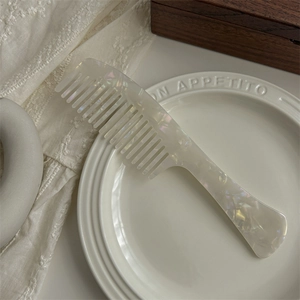 Macro shot of large wide-tooth acetate comb with pearlescent marble texture on ceramic plate