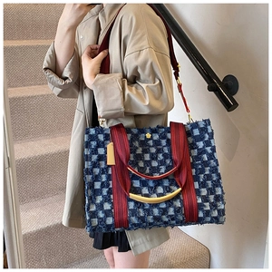 Detail of checkered denim tote bag with frayed edges and red shoulder strap on a model