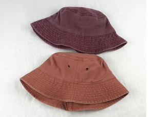 Top view of two washed cotton bucket hats in dark burgundy and orange-brown on white fabric