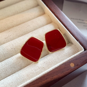 Detailed macro view of red enamel earrings with gold borders in a wooden jewelry box