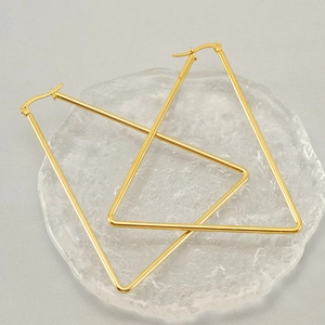 Close-up of gold geometric triangle hoop earrings on a textured glass plate