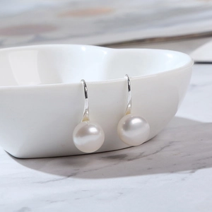 Macro shot of white pearl drop earrings hanging on a white heart-shaped ceramic bowl