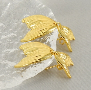 Macro detail of gold fishtail earrings with vertical textures on a textured glass tray
