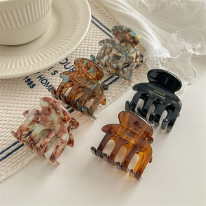 Five French style acetate hair claws in various marbled colors on a soft fabric background