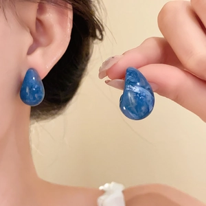 Macro detail of blue marble teardrop earrings with elegant white stone resin textures