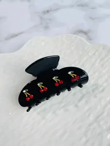 Detail of a black hair claw clip featuring red and green rhinestone cherry patterns