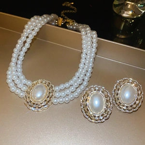 Detailed view of luxury three-layer pearl necklace and matching gemstone earrings on a tray