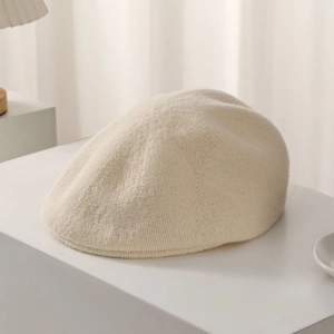 Detail of soft cream knitted beret showing thick wool texture on white pedestal