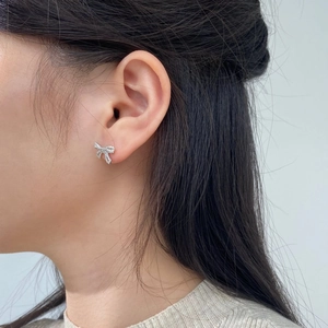 Detail of sparkling crystal bow stud earrings worn by a model on a grey background