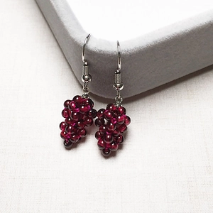 Macro shot of handmade wine red garnet grape earrings hanging on a gray jewelry box