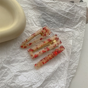 Detailed view of three resin hair clips with cream base and red confetti accents