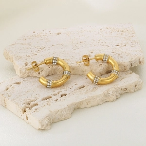 Détail de boucles d'oreilles dorées en C géométrique avec trois rangées de zircons blancs