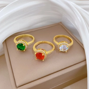 Adjustable gold rings set with green, red, and white cubic zirconia on silk fabric