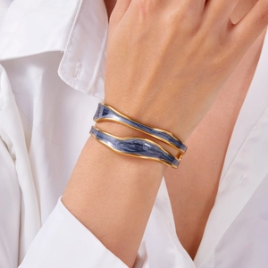 Detail of gold-framed irregular bangle with blue-grey enamel inlay on a white sleeve