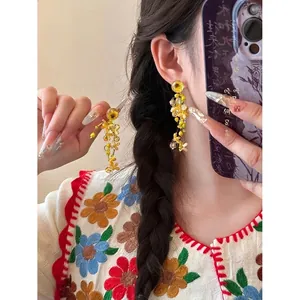 Close-up of yellow flower tassel earrings with intricate beads on a female model