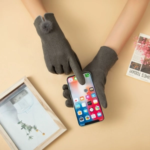 Primer plano de guantes térmicos grises para mujer con pompón usando una pantalla táctil