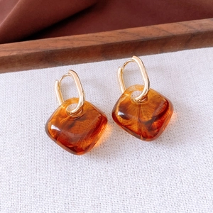 Macro view of amber acrylic square pendant earrings on vintage fabric background